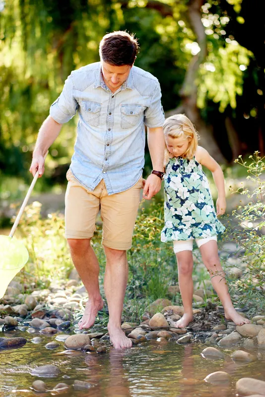 Father and daughter wading in creek