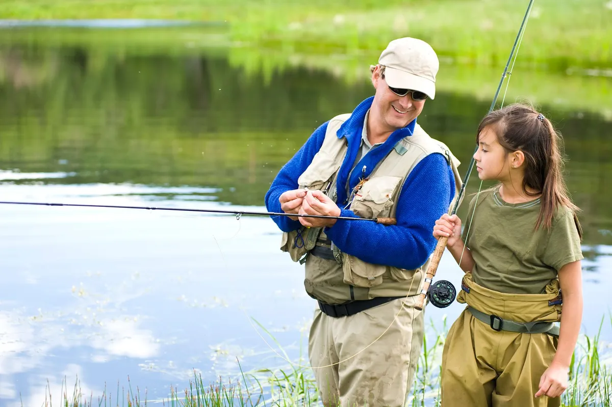 Father and daughter fly fishing at pond